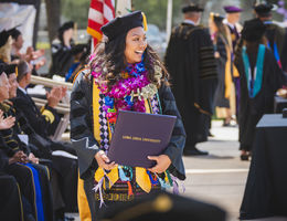 Female graduate in cap and gown wearing floral lei after accepting degree.
