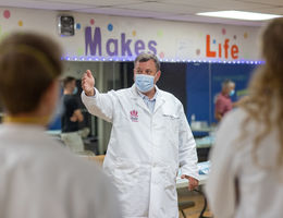 Caucasian doctor stands in white coat with hand outstretched guiding people.