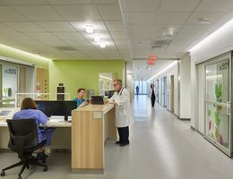 hospital hallway, male caucasian doctor with white beard and glasses in white coat standing at nurse station talking to male caucasian nurse in blue scrubs who is sitting