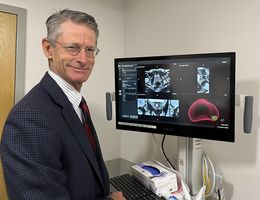 Caucasion man in suit standing next to medical scans related to prostate cancer on a computer monitor