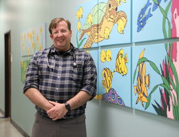 Dr. Daniel Lamb stands in hallway in front a painting of turtles and fish