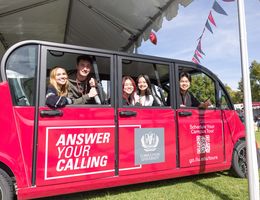 College students in a red, over-sized golf cart, smiling at the camera