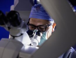 Male doctor in glasses looks through microscope in preparation for brain tumor surgery