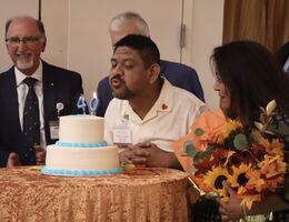A man blows out candles on a two tiered cake with people surrounding him.