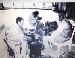 black and white photo showing three military men sitting with combat gear surrounding them.