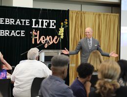 A man in a grey suit stands in front of the crowd and gives a sermon about embracing hope