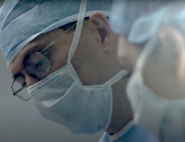 A close up if two doctors with blue face masks and blue net caps in an operating room