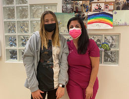 tall female patient poses for photo, hugging smiling female doctor in scrubs
