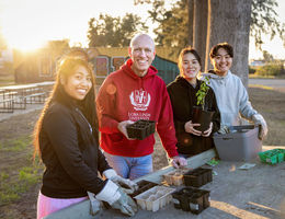 four individuals smiling, gardening at a table outside in hoodie sweatshirts