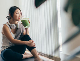 Woman taking a break from exercise to drink a green smoothie