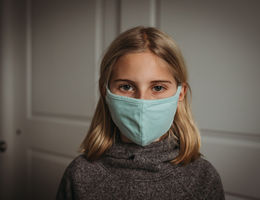 Girl in face mask looking at camera during Covid-19 pandemic - stock photo