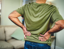 Cropped shot of a senior man in a green shirt holding his lower back suffering from back pain