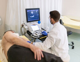 Doctor looking at the computer screen while doing an ultrasound test of a senior male patient lying on clinic bed during pandemic. Cardiologist doing heart ultrasound of an elderly man in hospital.