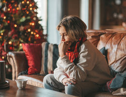 Person in white sweater on the couch sitting in sadness at home during Christmas