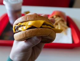 A young man is holding a piece of hamburger in his hands. The concept of unhealthy food, diet, overeating, gluttony, dependence on food. Fast food restaurant, snack bar. 