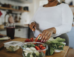 Midsection of young woman cutting red bell pepper while preparing salad in kitchen at home