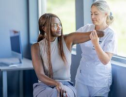 A black woman amputee and a white nurse stretch her arm