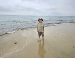 A female stands in the sand on the beach on an overcast day with the ocean water behind her