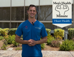 A white doctor in blue scrubs stands in front of a medical building outside and talked to the camera.