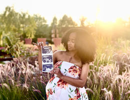 African American woman stands with sonogram in front of field, pregnant and smiling