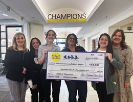 six women smiling at the camera holding a large check