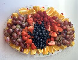 A tray of grapes, oranges, strawberries, and blueberries sitting on a white table