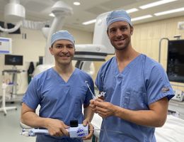 Structural interventional cardiologists Drs. Amr Mohsen (left) and Jason Hoff (right) hold the device they used to perform Gail Perszyk's mitral transcatheter edge-to-edge valve repair.