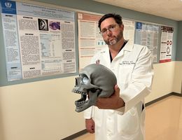 Jared Inman, MD, a head and neck surgical oncologist at Loma Linda University Health, holds a 3D replica of a human skull, around which various cancers can form.