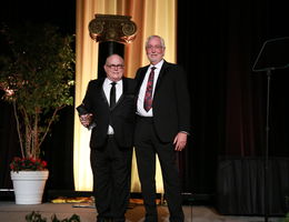 two doctors standing on stage, one holds award, both smiling