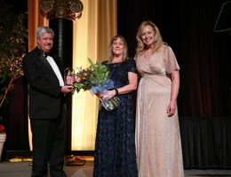 senior vice president for advancement, Rachelle, stands with Don and Penny holding award and flowers smiling for photo on stage