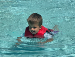 Young boy swims in pool with US Coast-guard approved life vest