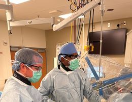 Two doctors in blue scrubs standing over a patient during a surgery 