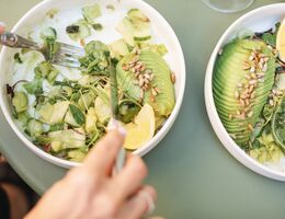Overhead view of a woman eating a green salad with avocado, cucumber and toasted sunflower seeds 