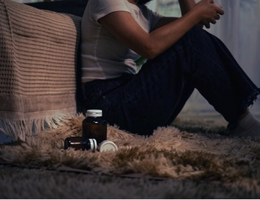 teen sits on floor by bed with bottle of pills closeby