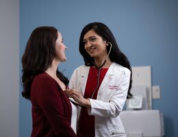 a woman doctor uses here stethoscope to examine a woman patient