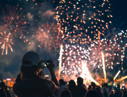  The back of a girl in a baseball cap filming a fireworks display on her mobile phone
