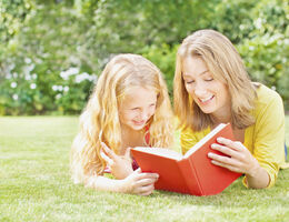 Mother reading to daughter in backyard