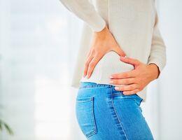 A woman in a white sweater and jeans holds her hip with pain
