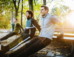 young men are leaning on a bench and stretching in a wooded forest 