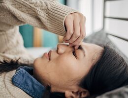 A woman having headache while lying on bed in her bedroom at home