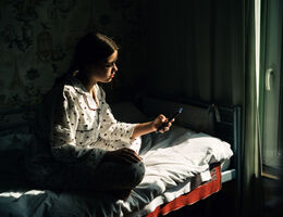 teenage girl looks at phone while in bed