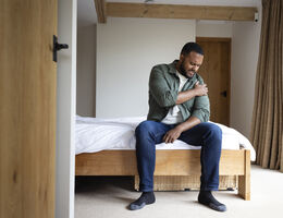 A mid adult man sitting on the edge of his bed in the bedroom at home