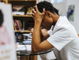 Side view of stressed teenage boy sitting with head in hand at library of school