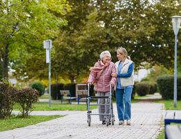 Senior woman and her home caregiver spending a chilly, windy day outdoors in city park. Autumn walk for elderly patient with walker