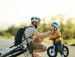 A father kneeling down to strap on a helmet for a young boy