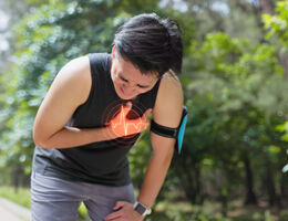 young man in park bends down by roadside and suffers from chest pain 