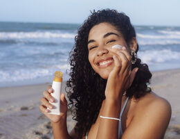 Young woman applying sunscreen on her face at the beach