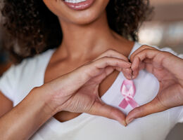 Women wearing pink ribbon on chest and making a heart with her hand
