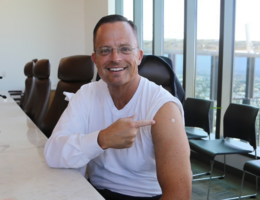Man in white shirt points to bandaid on his arm