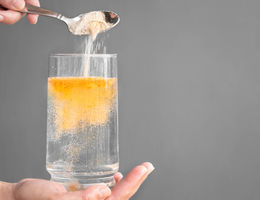 Pouring orange powder, alluding to electrolyte supplements, into clear water glass